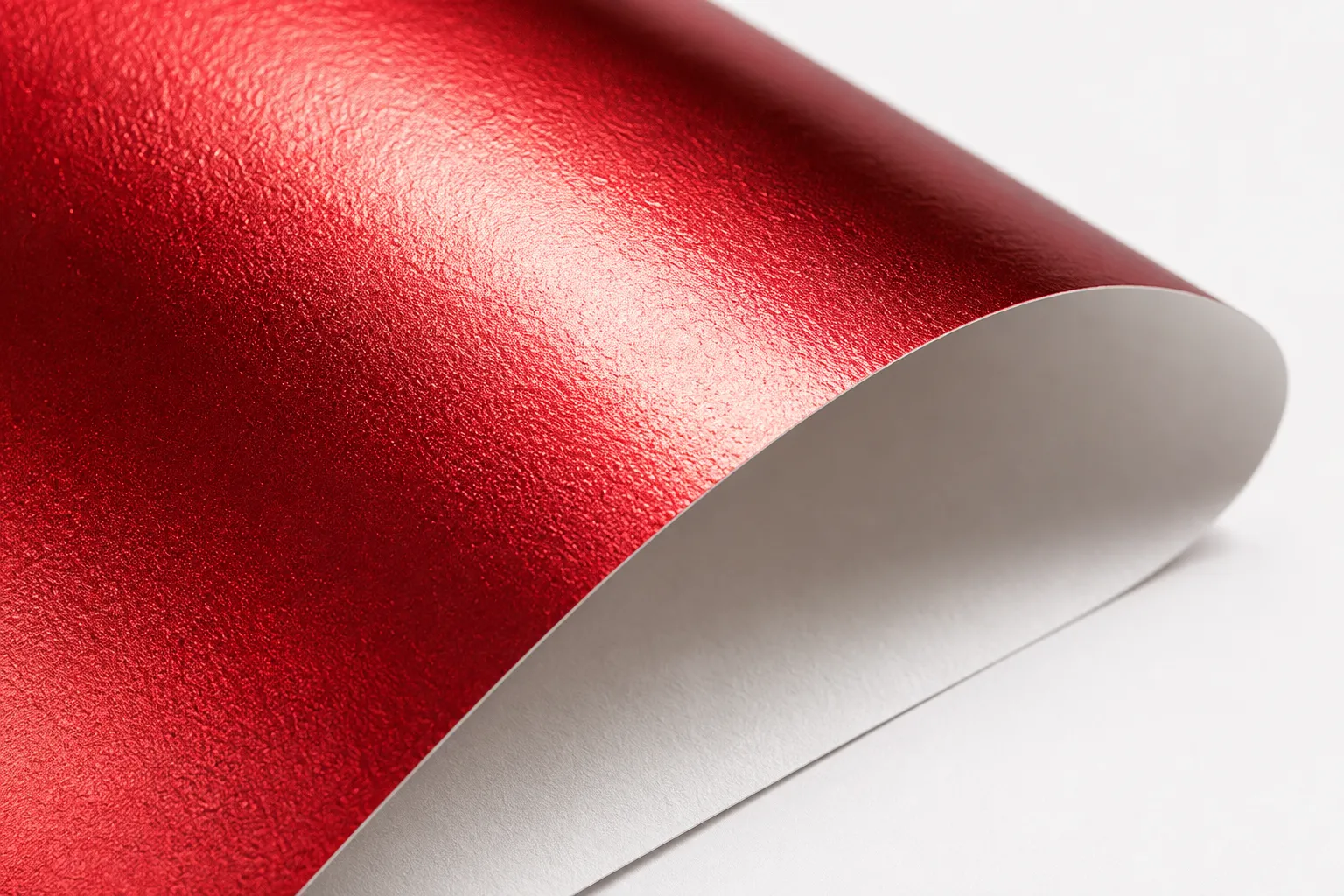 Macro d'un papier métallisé rouge se recourbant sur une feuille blanche